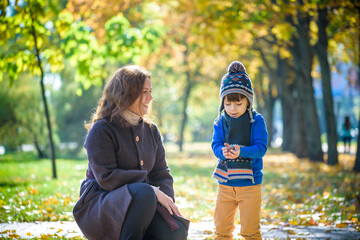 Mother and baby play in autumn park. Parent and child walk in the forest on a sunny fall day. Children playing outdoors with yellow maple leaf. Toddler boy play with golden leaves. Mom hugging kid