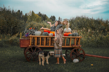 Obraz premium Beautiful happy family, mother, daughter and pet dog together, on a wooden cart with colorful pumpkins
