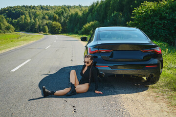 Racer woman sits on asphalt and leaning to her powerful racing car