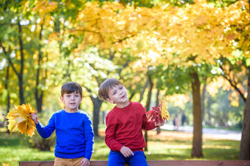 happy friends, schoolchildren having fun in autumn park among fallen leaves