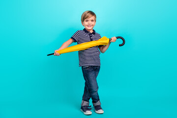 Full body photo of nice little boy hold umbrella wear t-shirt jeans sneakers isolated on teal background
