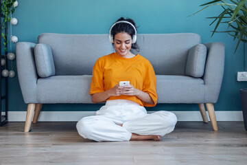 Motivated young woman listening to music with smartphone while dancing sitting on the floor at home.