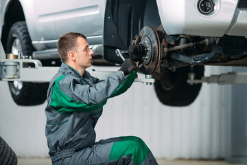 Car lifted in automobile service for fixing, worker repairs the wheel,