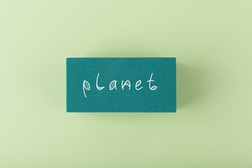 Planet handwritten on dark green rectangle against light green background. Concept of planet, eco friendly life style, plastic, pollution or ecological problems
