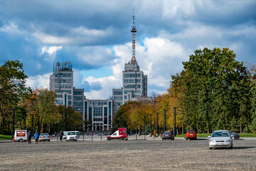 Fototapeta na wymiar Kharkiv, Ukraine - October 20, 2020: View of Derzhprom building among yellow autumn trees on Svobody Square in Kharkiv. Urban landscape with Soviet skyscrapers on the backdrop of a dramatic cloudy sky