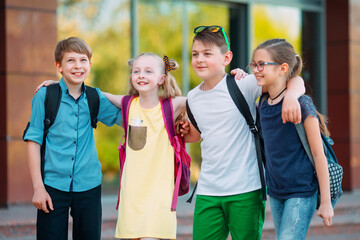 Children's friendship. Four little school students, two boys and two girls, stand in an embrace on the schoolyard.