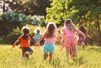 Large group of kids, friends boys and girls running in the park on sunny summer day in casual clothes . - obrazy, fototapety, plakaty
