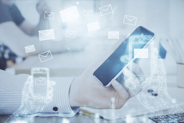 Double exposure of man's hands holding and using a digital device and envelop hologram drawing. E-mail concept.