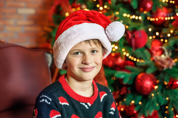 boy in Santa hat at home near christmas tree. Happy child waiting for christmas