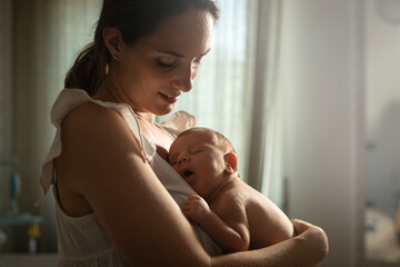 Authentic of young peaceful neo mother cuddling newborn baby while sleeping on her arms in nursery...