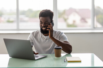 African black man talking on mobile cell phone to clients in office with laptop computer