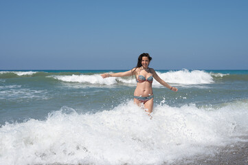 Young woman in a white shirt is bathes in the waves in the sea foam on an exotic tropical island