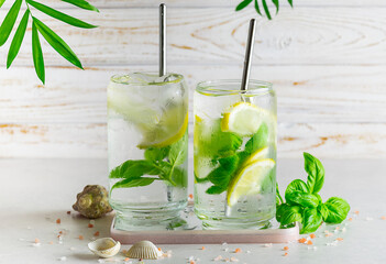 Refreshing iced cocktails with lemon and basil in transparent glasses on white wooden background...