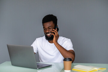 Joyful african american businessman talking on phone, laughing and drinking coffee at workplace in office