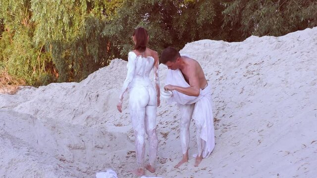 Man covers a woman's body with white paint. He puts bodypainting on the body.
