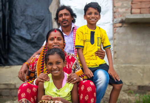 Indian Rural Parents and their two children sitting in front of the family house in village