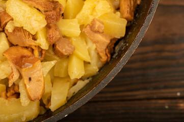 Potatoes fried in a frying pan with mushrooms on a wooden table. A traditional village dish.