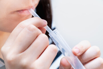 PCR検査キットを使用し、自宅で唾液を採取する女性の写真。PCR検査のイメージ。 - obrazy, fototapety, plakaty
