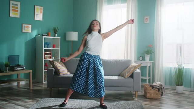 Young woman with long hair in green skirt and white top, ballet dancer is practicing at home, learning dance alone in isolation, getting ready to performance, Slow motion.