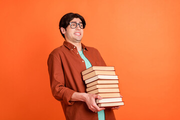 Photo of young happy smiling funky funny guy college student hold heavy books wear glasses isolated on orange color background