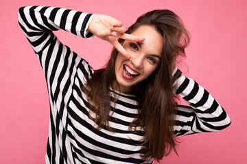 Photo of young european positive smiling winsome happy funny beautiful brunette woman with sincere emotions wearing casual striped pullover isolated on pink background with copy space