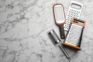 Different modern graters on white marble table, flat lay. Space for text