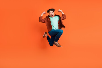 Fototapeta na wymiar Full size photo of happy excited funky funny guy jumping showing muscles victory isolated on orange color background