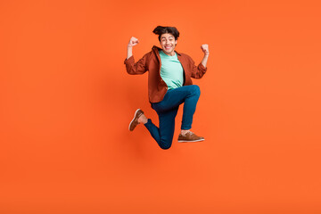 Full size photo of smiling cheerful young man jumping raise fists in victory triumph isolated on orange color background