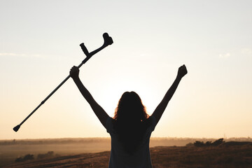 Fototapeta premium Woman holding elbow crutch outdoors at sunrise, back view. Healing miracle