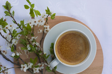 A cup of coffee, a book and blooming cherry branches on a white tablecloth. White sakura. Atmosphere, comfort, rest
