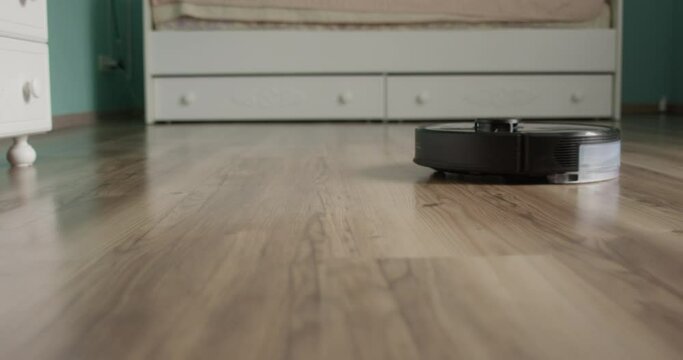 Robot Vacuum Cleaner is Mopping a Laminated Floor in a Room of Teenager
