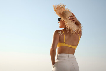 Young woman with sun protection cream on shoulder against blue sky, back view