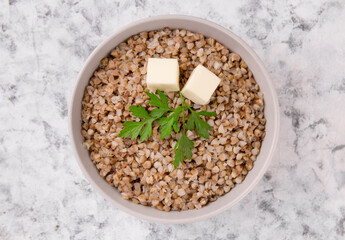 Boiled buckwheat in a plate with parsley leaf and butter on a white.