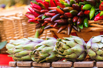 Fresh green artichokes with green leaves and bunches of red and green hot chili peppers in a basket...