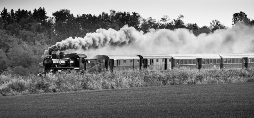 Steam train runs on the tracks in the countryside. Black and white photography.