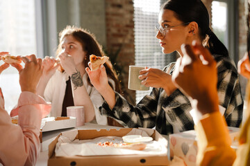 Multiracial young women eating pizza while having break