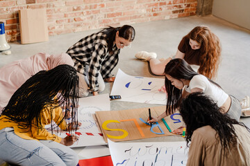 Multiracial young feminist women making posters during meeting