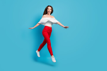 Fototapeta na wymiar Photo of adorable impressed young woman dressed white blouse smiling jumping high empty space isolated blue color background
