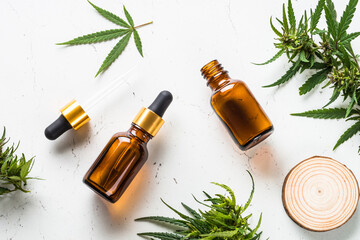 CBD oil and cannabis leaves at white table. Medicine and cosmetic product. Flat lay image.