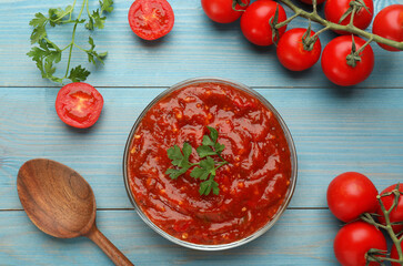 Delicious adjika sauce in bowl and ingredients on light blue wooden table, flat lay