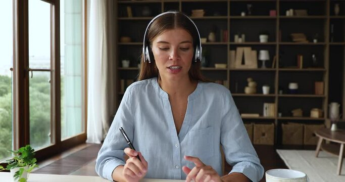 Screen view portrait of teenage female presenter in earphones look at camera talk in videochat. Motivated young lady work seeker shoot video business card speak before webcam on distant job interview