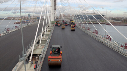 Above view of workers and machinery laying asphalt on highway bridge