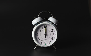 Front view of white  vintage alarm clock shows12 o clock  on black background.