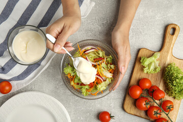 Woman adding mayonnaise to delicious salad at grey table, top view