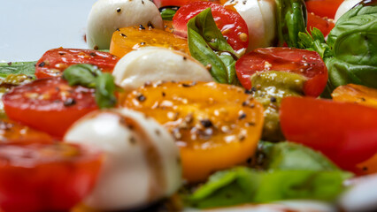 Defocused foreground of caprese salad. Healthy meal with cherry tomatoes, mozzarella balls, spices and basil.
