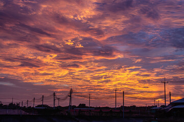 The image of the orange sky in the evening before the sun sets b, electric cables and a house roof., with light poles