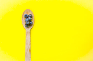 Flat lay of recycled spoon and juicy, fresh blueberries on color table. Space for text. Isolated ripe sweet bilberry fruits in eco spoon on yellow background. Copy Space. Healthy raw vegetarian food 