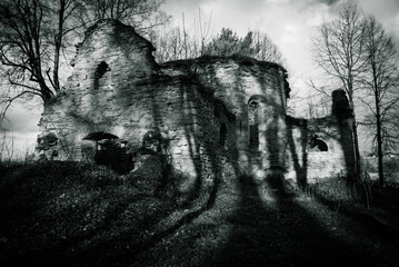 Creepy ruins of a medieval church with long, evening shadows cast by the trees. Gothic atmosphere from Eastern Europe. 