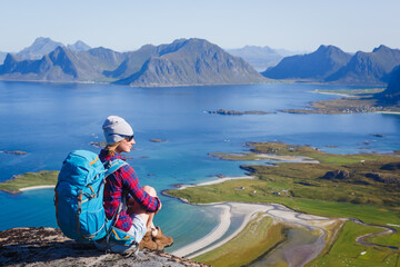 Woman hiker relaxing at the top of the mountain and looking at incredible views of a Norwegian fjord, Lofotens. Travel, adventure, healthy lifestyle concept