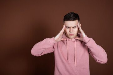 Portrait of a young guy suffering from migraines. Brown background.